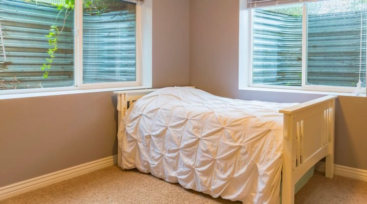 Interior view of a newly installed double-hung egress window in a finished basement bedroom; white frame, sheer blinds, natural light filtering through greenery outside—enhancing safety, ventilation, and aesthetics.