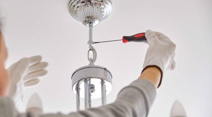 Close-up of a technician in white gloves using a screwdriver to secure a polished chrome chandelier with ornate ceiling canopy—highlighting precision electrical and finish work by Teton Repair & Remodel.