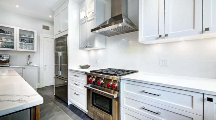 Bright, high-end kitchen with white shaker cabinets, marble island countertop, stainless steel range and hood, subway tile backsplash, glass-front upper cabinets, and dark gray porcelain floor tiles—exemplifying clean, functional design.